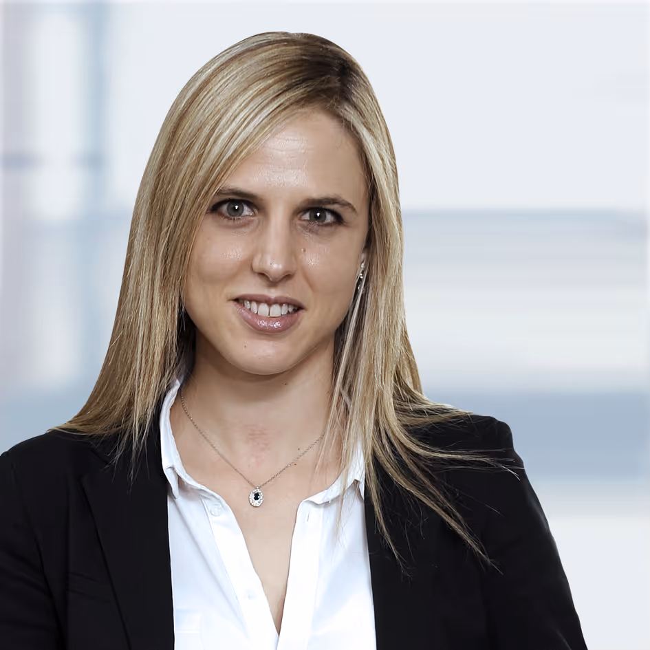 Portrait of a woman with straight blonde hair wearing a black blazer, white shirt, and a pendant necklace, smiling softly.