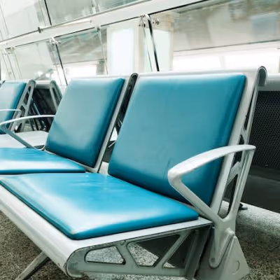Empty teal cushioned chairs with metal armrests in a waiting area.