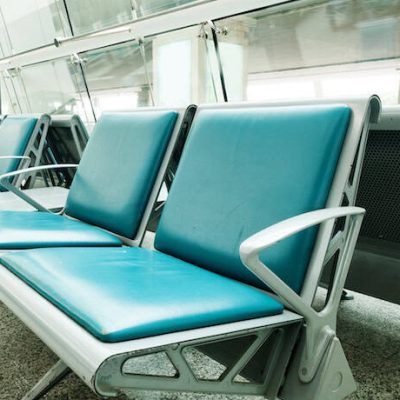 Empty teal cushioned chairs with metal armrests in a waiting area.