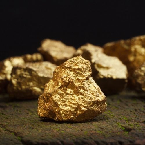 Close-up of raw gold nuggets on a dark surface with a black background.