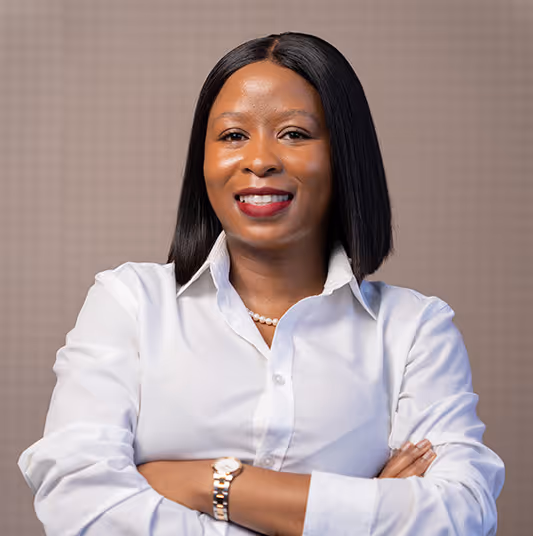 Confident woman with shoulder-length straight black hair, wearing a white button-up shirt and pearl necklace, smiling with arms crossed.