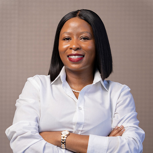Confident woman with shoulder-length straight black hair, wearing a white button-up shirt and pearl necklace, smiling with arms crossed.