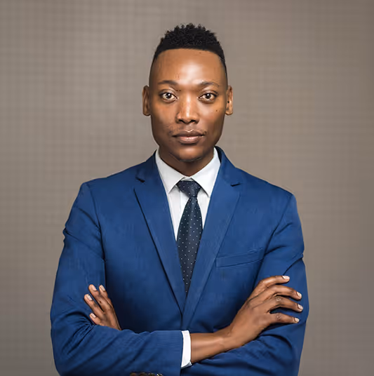 Confident man in a blue suit with a white shirt and black tie standing with arms crossed.
