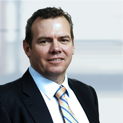 Portrait of a man in a dark suit, white shirt, and striped tie, smiling slightly against a blurred office background.