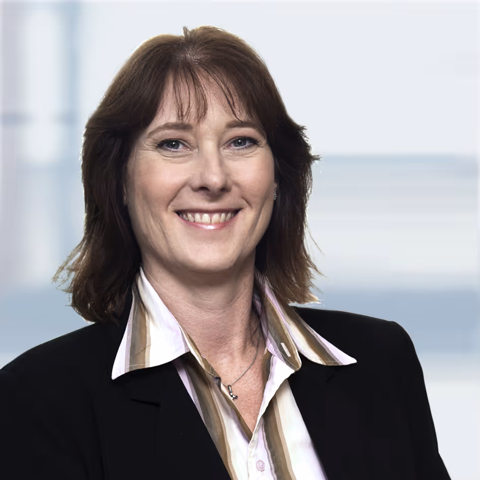 Smiling woman with brown hair wearing a black blazer and striped shirt against a blurred background.