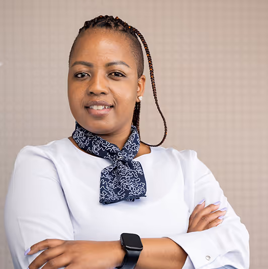 Confident woman with braided hair wearing a white blouse and patterned scarf, arms crossed, and smartwatch on wrist.