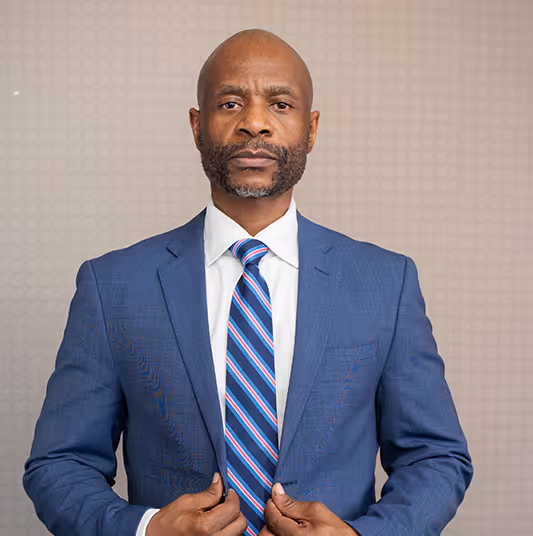 Confident man in a blue suit and striped tie adjusting his jacket against a light patterned background.