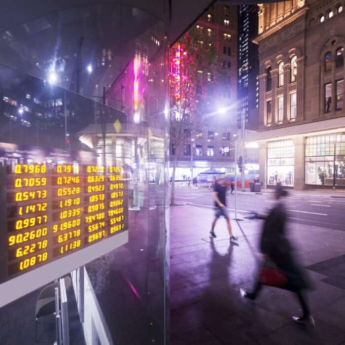 Night city street scene with blurred pedestrians and a reflective glass panel displaying bright yellow financial numbers.