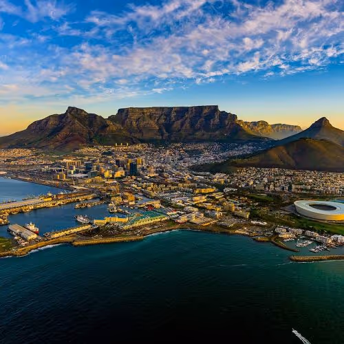 Aerial view of Cape Town with Table Mountain in the background, ocean in the foreground, and cityscape scattered across the coast.