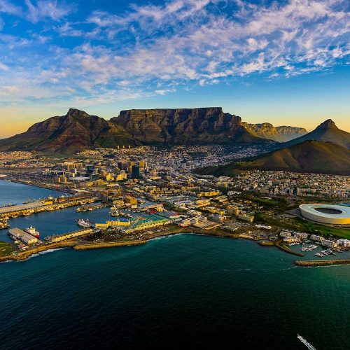 Aerial view of Cape Town with Table Mountain in the background, ocean in the foreground, and cityscape scattered across the coast.