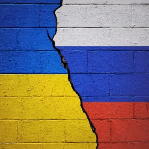 A cracked wall painted with the Ukrainian flag on the left and the Russian flag on the right, the crack running vertically between them.