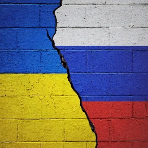 A cracked wall painted with the Ukrainian flag on the left and the Russian flag on the right, the crack running vertically between them.